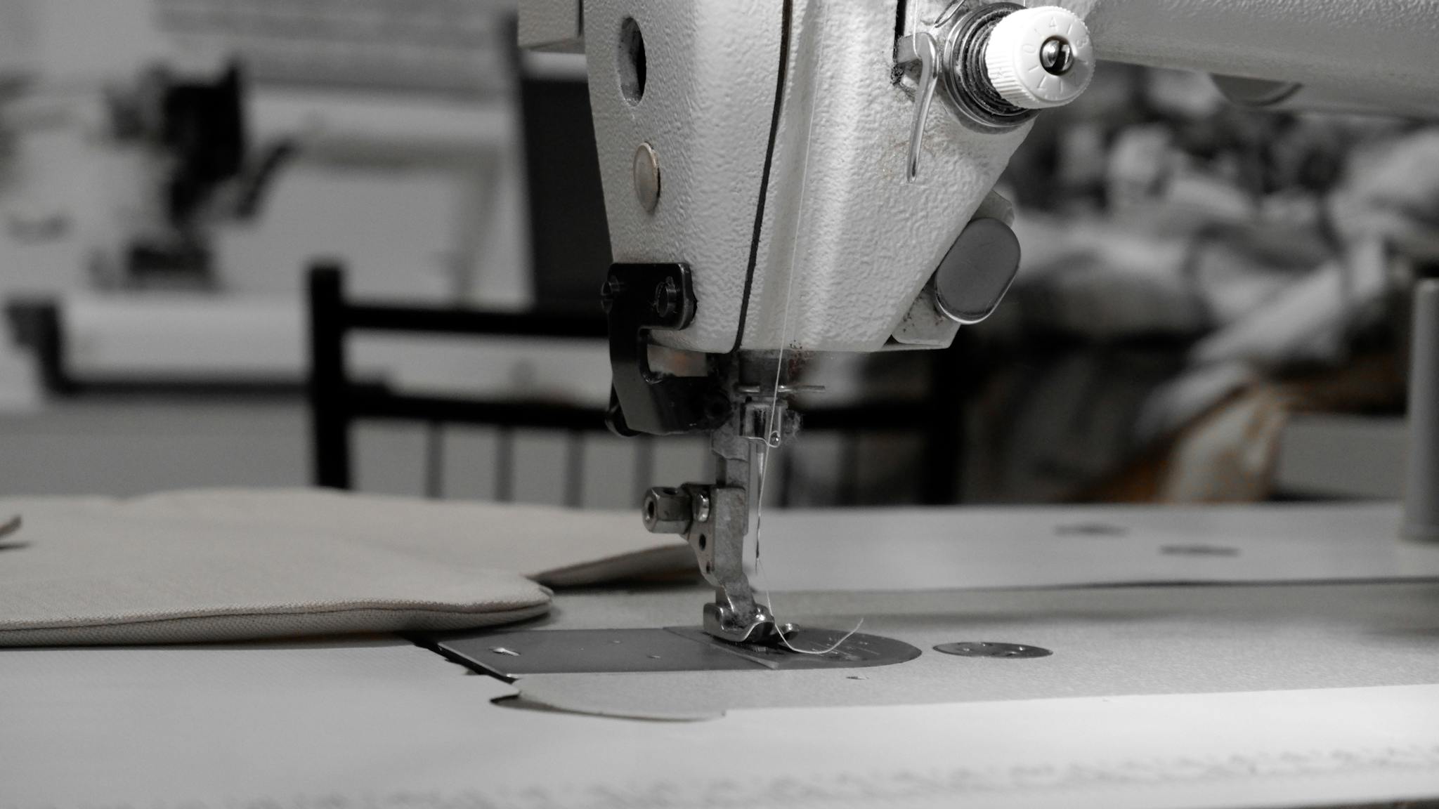 Closeup of an industrial sewing machine in a textile factory, focused on needle and fabric.