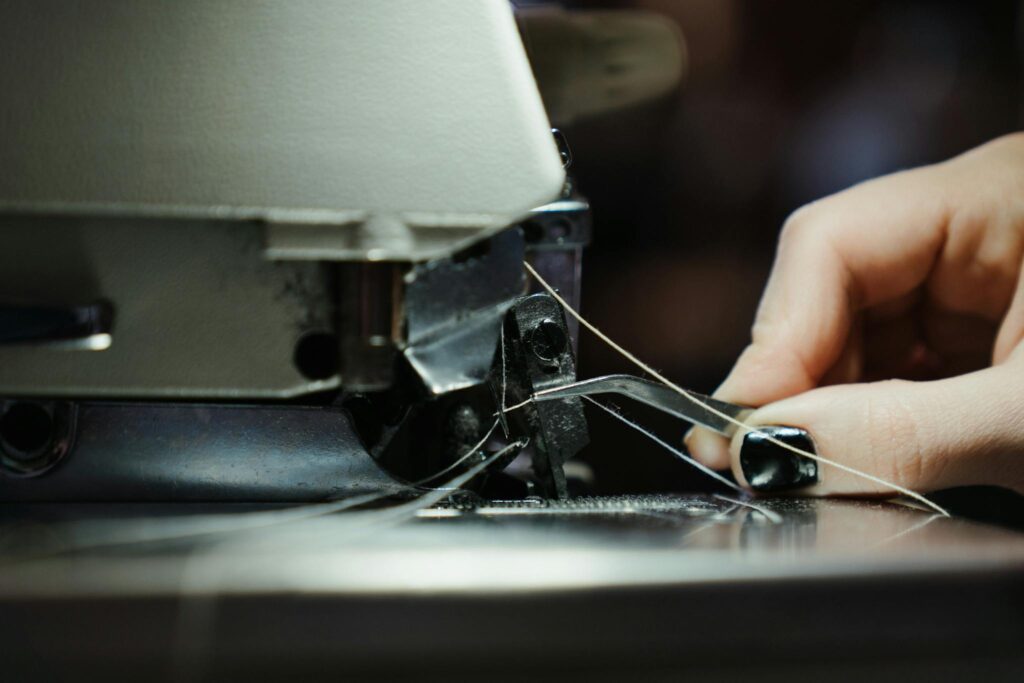 Detailed close-up of a sewing machine in use, highlighting the threading process with a human hand.
